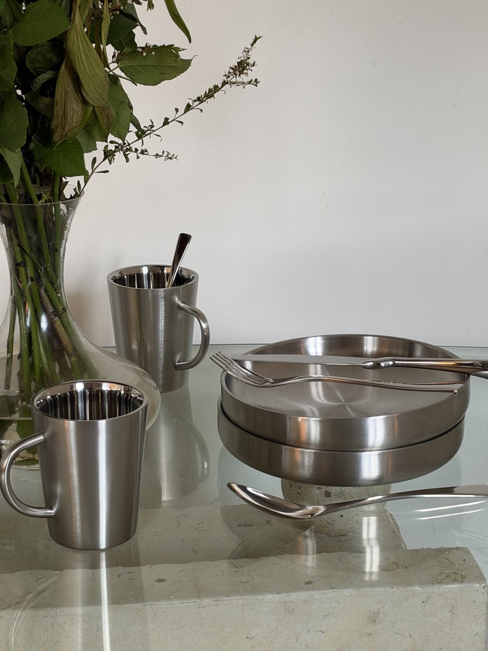 NovaChrome steel tableware arranged beside a glass vase on a mirrored table